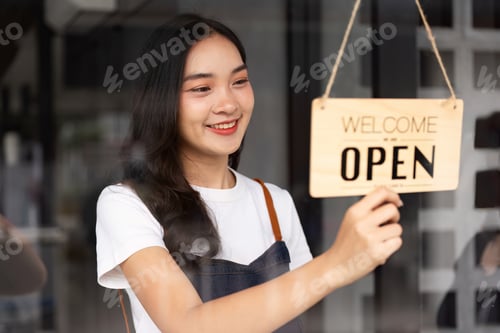 Preview: Friendly Coffee Shop Staff Member Hanging Open Sign at Modern Cafe Entrance