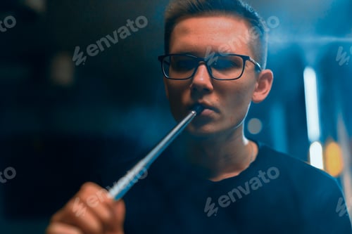 Preview: A man in glasses smokes a traditional hookah pipe A man exhales thick smoke in a hookah cafe
