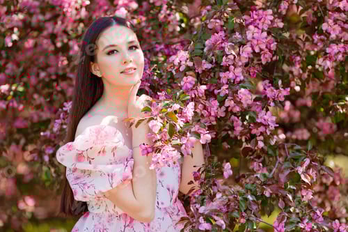 Preview: A charming girl in a pink dress standing near pink blooming garden