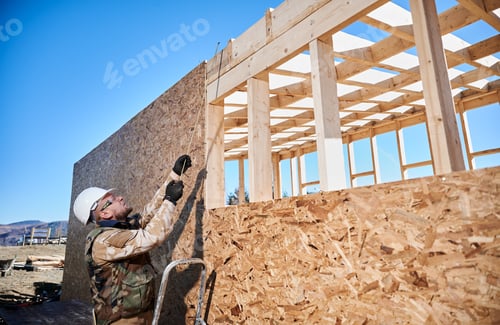 Preview: Man worker building wooden frame house on pile foundation.