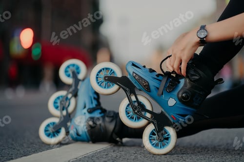 Preview: Cropped shot of unrecognizable woman puts on rollerblades poses outdoors on asphalt