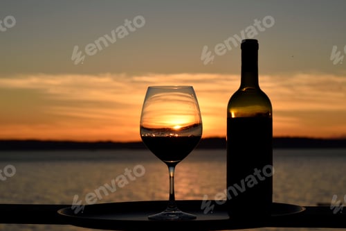 Preview: Sunset wine glass and bottle outside deck table.