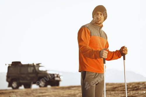 Preview: Man traveler with trekking sticks going up the mountain
