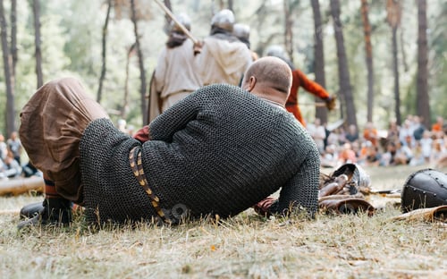 Preview: Unrecognizable ancient warrior in chain mail resting lying on the grass, close-up, rear view