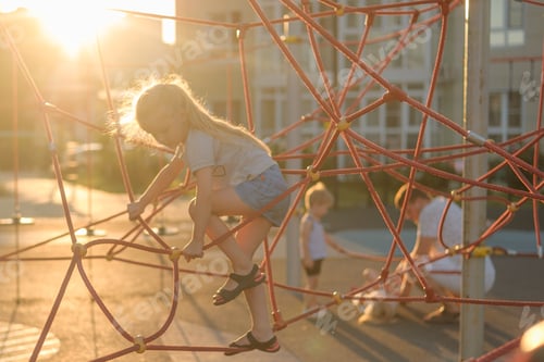 Preview: girl climbs a rope on a construction spider web on a playground on a warm summer evening in a golden