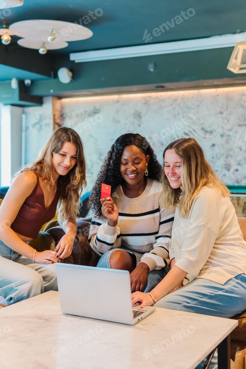 Preview: A multi-ethnic group of friends shops together online using a laptop in a coffee shop.