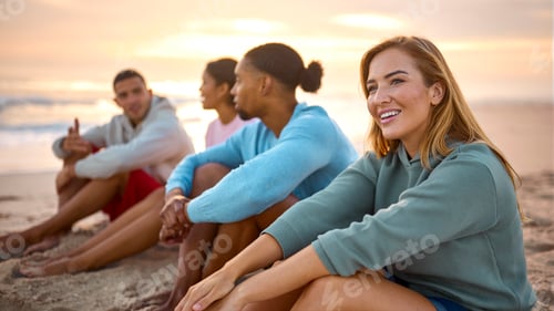 Preview: Young Couple With Friends In Casual Clothing On Vacation Sitting On Beach Watching Sunrise Together