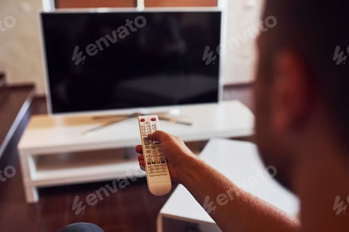 Preview: Backing view of man holds remote controller in hand and turning on TV