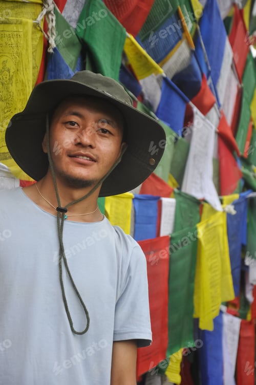 Vista previa: A Asian young guy looking at camera, standing against Buddhist prayer flags