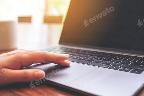 Preview: Closeup image of a hand using and touching on laptop touchpad with coffee cup on wooden table