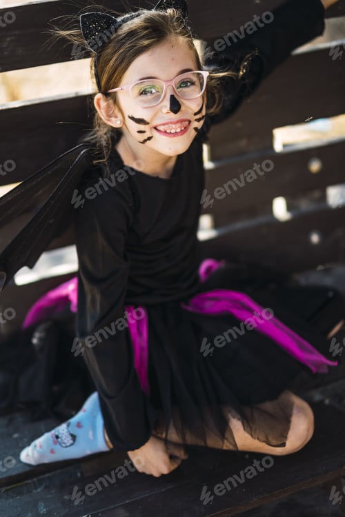 Preview: Cute little girl wearing a Halloween cat costume and sitting on a bench