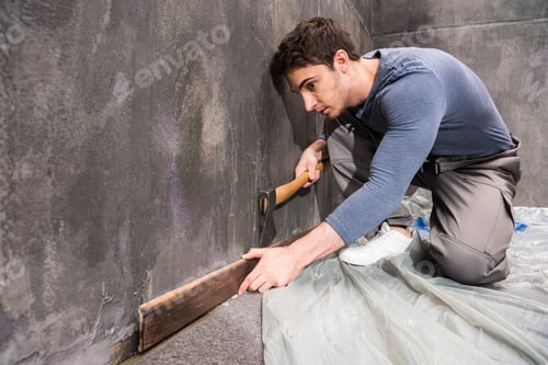 Preview: Professional young handyman with axe repairing floor, renovation concept
