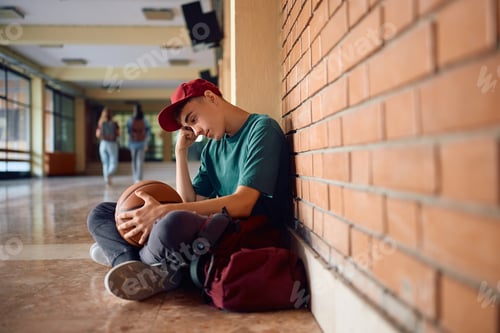 Preview: Sad teenage boy sitting alone at high school hallway.