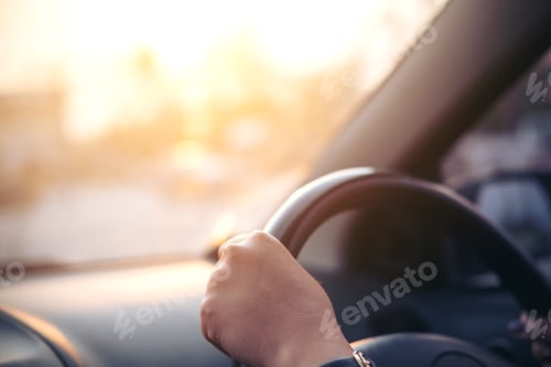 Preview: Woman's hands holding on black steering wheel while driving a car during sunset