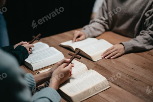 Preview: Group of Christians sit together and pray around a wooden table with blurred open Bible pages