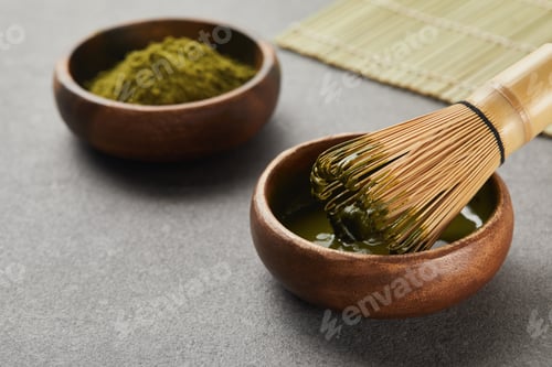 Preview: selective focus of matcha powder bowl near bamboo whisk in green tea