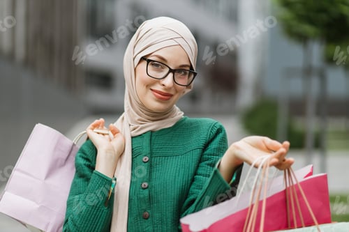 Preview: Muslim womanenjoying her walk and shopping in the city, smiling and holding colorful shopping bags.