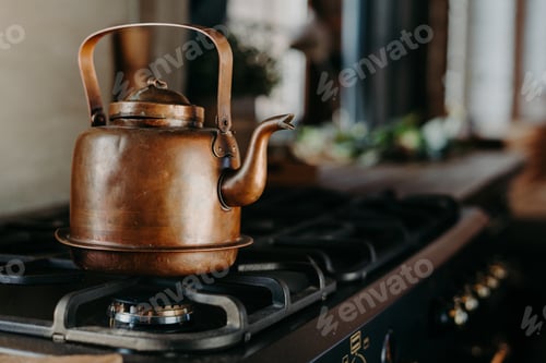 Preview: Bronze kettle in modern kitchen. Old vintage teapot on gas stove. Preparing tea