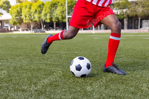 Preview: An African American young male athlete, a soccer player in red and white uniform, is kicking a ball