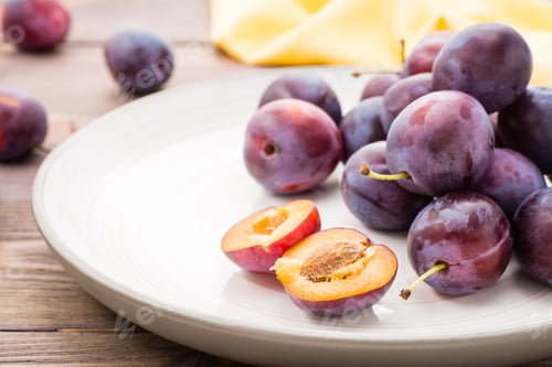 Preview: Close-up of a broken ripe blue plum and whole berries on a plate on a wooden table