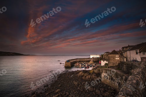 Preview: A beautiful landscape of a Cornish fishing village and harbour at sunset in Coverack, Cornwall
