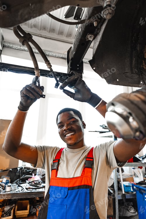 Preview: Young African mechanic in uniform working under the car in car service center