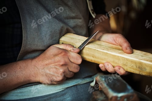 Preview: Close up of a craftsman cutting and paring the corners of a piece of wood with a sharp carving