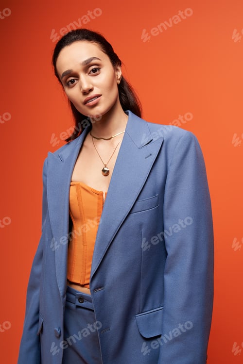 Preview: Stylish young woman in trendy blue suit and corset poses in vibrant studio setting