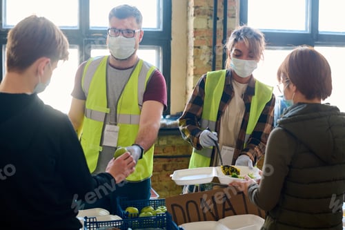 Preview: Man passing apple to boy while female putting food in container of refugee