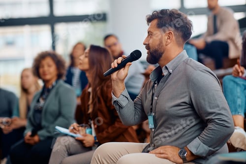 Preview: Business seminar attendee talking on microphone while sitting in the audience at convention center.