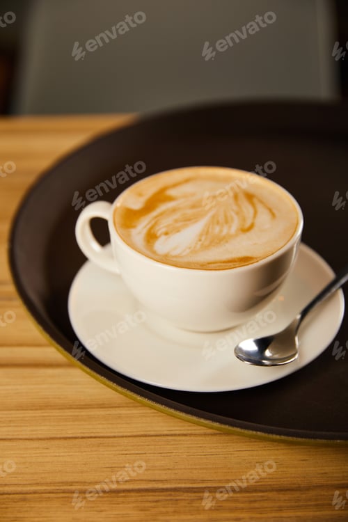 Preview: selective focus of cappuccino in white cup with saucer on black tray