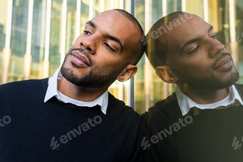 Preview: Black businessman leaning on glass wall of office building