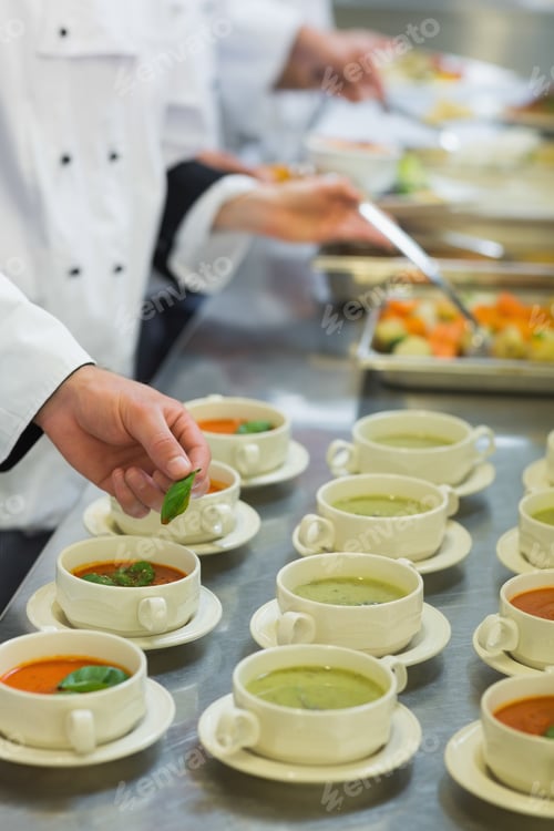 Preview: Bowls With Soup Being Garnished With Basil Leaves On Counter