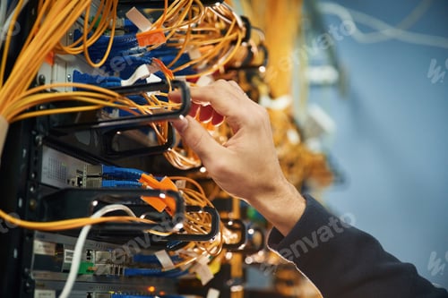 Preview: Young man is working with internet equipment and wires in server room