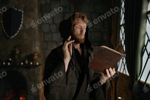 Preview: Medieval monk reading sacred religious book praying with rosary beads in hand
