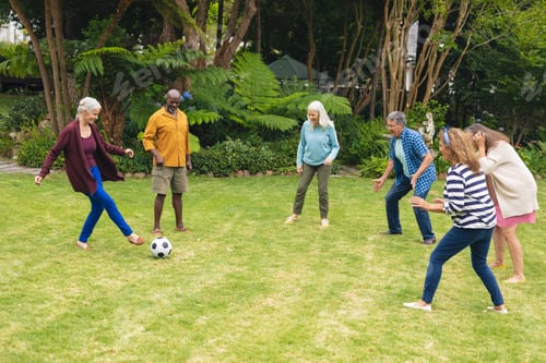 Preview: Multiracial active senior male and female friends playing soccer in backyard
