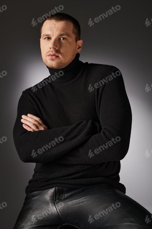 Preview: pensive charismatic trendy man in black sweater looking at camera on grey backdrop with lighting