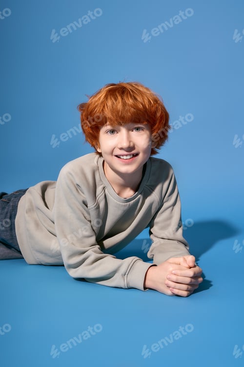 Preview: Charming young boy in stylish attire enjoys a playful moment on a vibrant blue backdrop