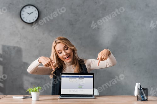 Preview: KYIV, UKRAINE - AUGUST 16, 2019: smiling businesswoman pointing with fingers at laptop facebook