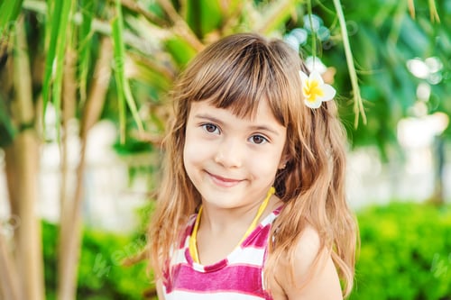 Preview: girl with a plumeria flower in her hair against the backdrop of palm trees. Selective focus.