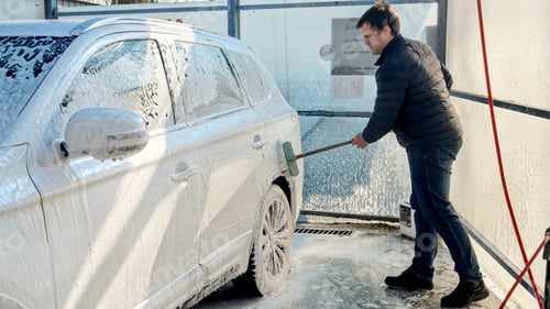 Preview: Young man washing his car with foam and brush at carwash. Automobile care, transport cleaning
