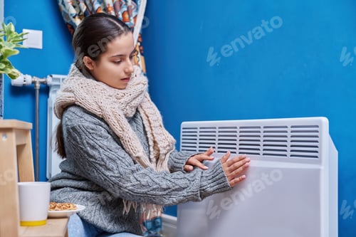 Preview: Teen female in sweater scarf warming near electric heating radiator