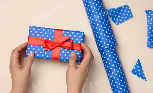 Preview: Female hands hold a blue gift box on a beige background