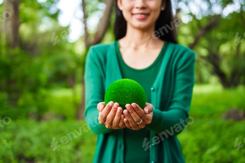 Preview: An Asian woman holds a globe in green forest,symbolizing importance preserving nature.emphasizes