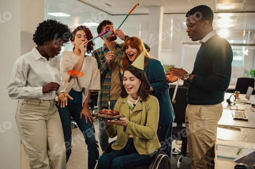 Preview: Happy businesswoman who uses a wheelchair blowing out a candle on cake at work