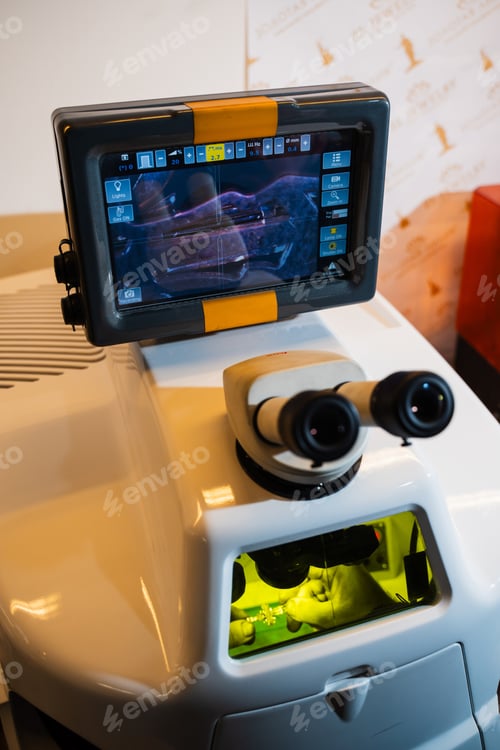 Preview: Artisan using a laser to join gold components in a dedicated chamber.