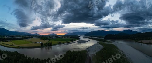 Preview: Fraser river by farm fields with mountains in background. Dramatic Sunset.