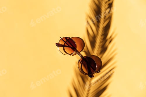 Preview: Shadow of palm branch falls on sunglasses against yellow background