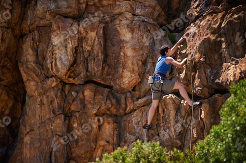 Preview: Hanging on tightly. A wide shot of a young woman rock climbing.
