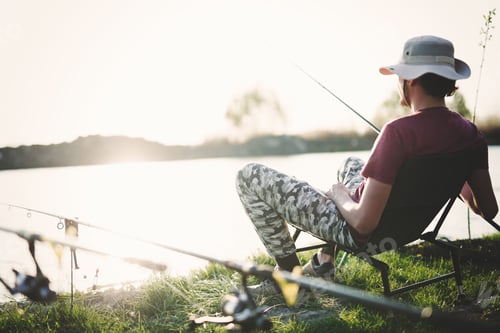 Preview: Young man fishing on lake at sunset enjoying hobby